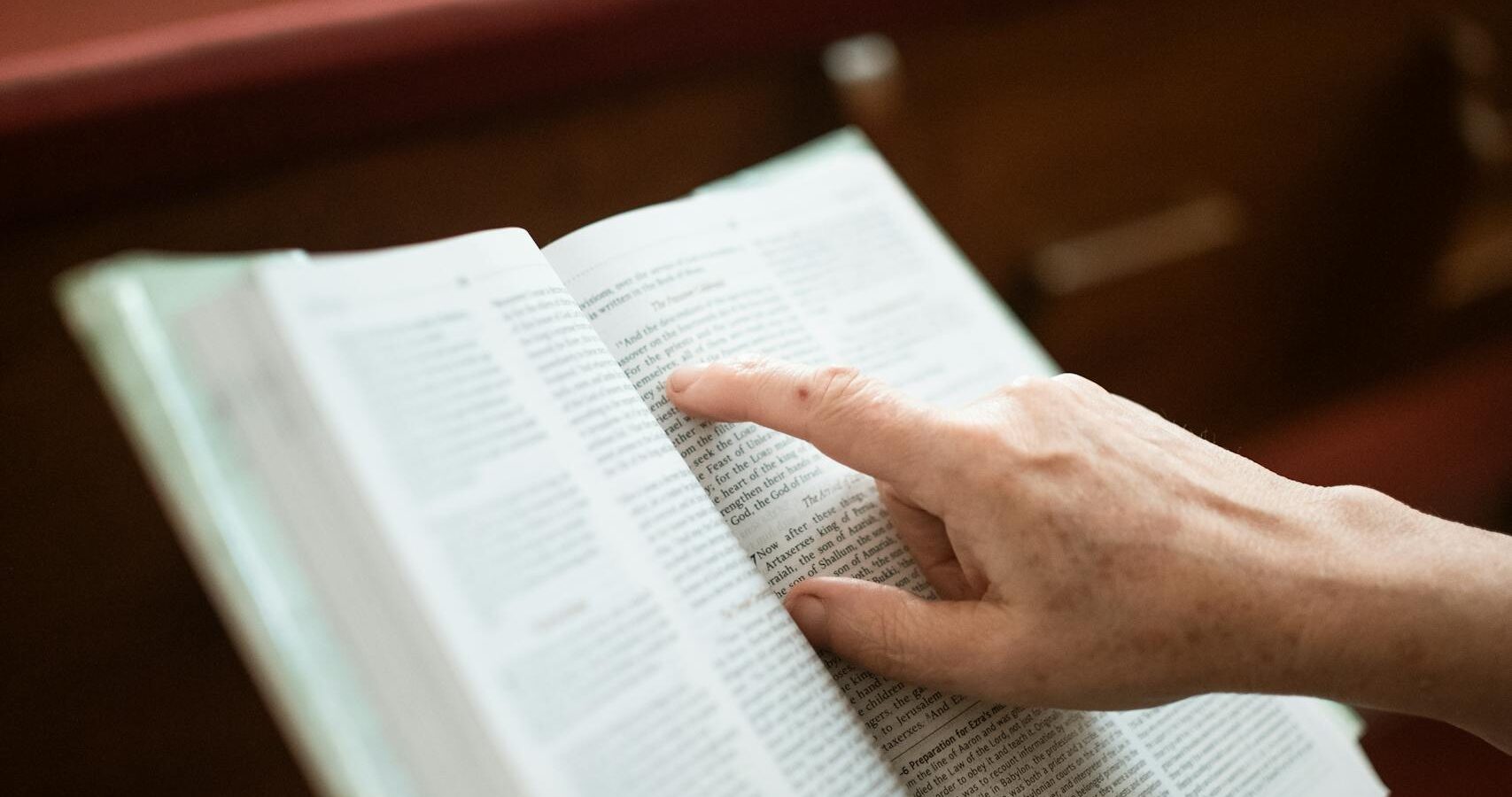 A close-up of hands holding an open Bible inside a church, symbolizing faith and devotion.